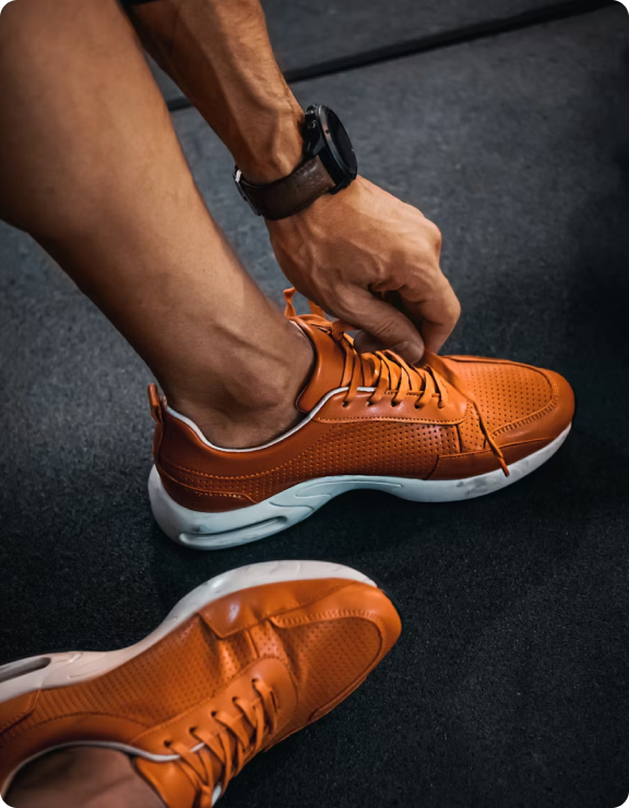 A man bending over to tie his orange running shoes. A Garmin watch is featured prominently on his left hand.