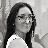 A black and white photo of a smiling woman. She has long dark hair and is wearing tortoise shell glasses.