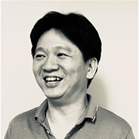 A black and white photo of a smiling man. He has dark hair and is wearing a polo shirt.